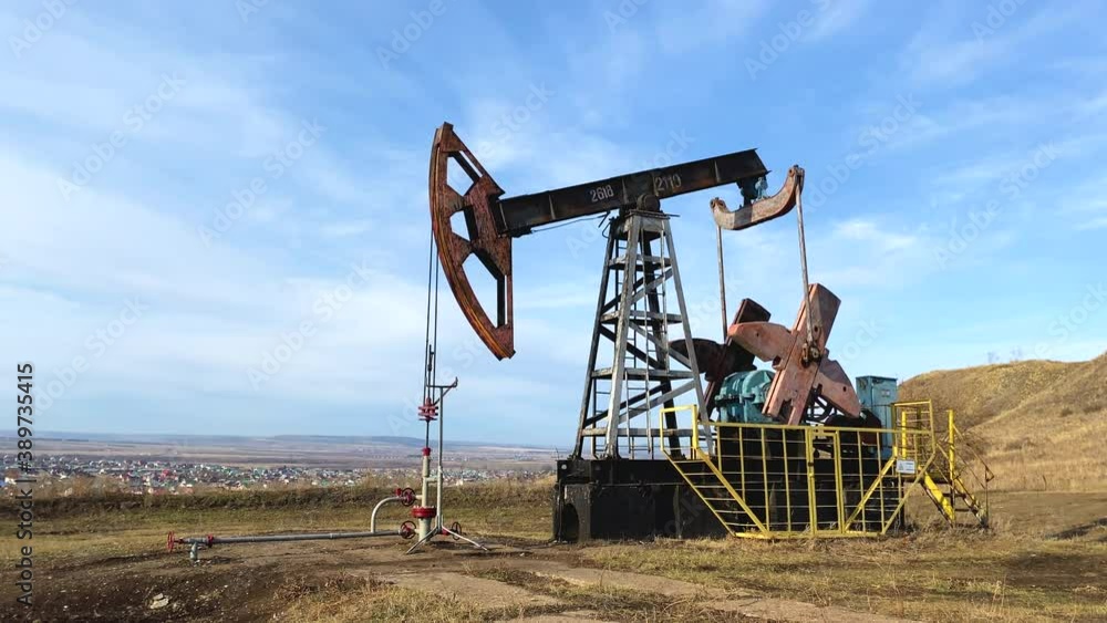 Machine for pumping oil and gas. Silhouette of a working oil pump from an oil field in the sun in a field. Industrial equipment. Side view. Machine for pumping oil and gas. Silhouette of a working oil pump from an oil field in the sun in a field. Industrial equipment. Side view.