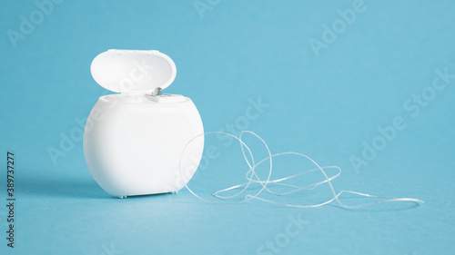 Container with dental floss. Floss on blue background. White dental floss case isolated. Open dental floss container