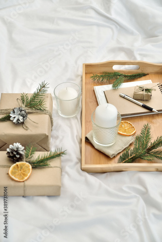 Cosy home flat lay composition with present boxes, blank copybook, a pen, tea and cones on a bed. Holiday shopping list, wish list or New Year Goals concept, presents checklist. Selective focus