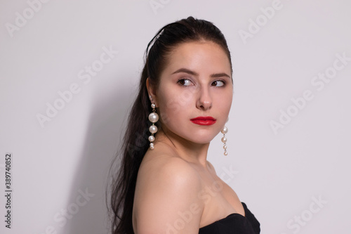 emotional portrait of attractive brunette in black top with white pearl earrings on white background.