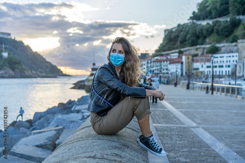 Mujer de 30 años dando un paseo  por una ciudad costera en tiempos de coronavirus llevando su mascarilla quirúrgica obligatoria photo