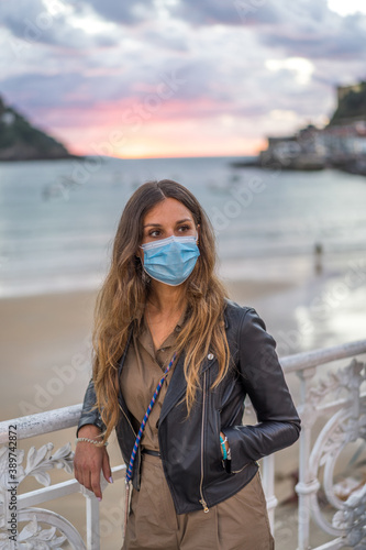 Mujer de 30 años dando un paseo  por una ciudad costera en tiempos de coronavirus llevando su mascarilla quirúrgica obligatoria photo