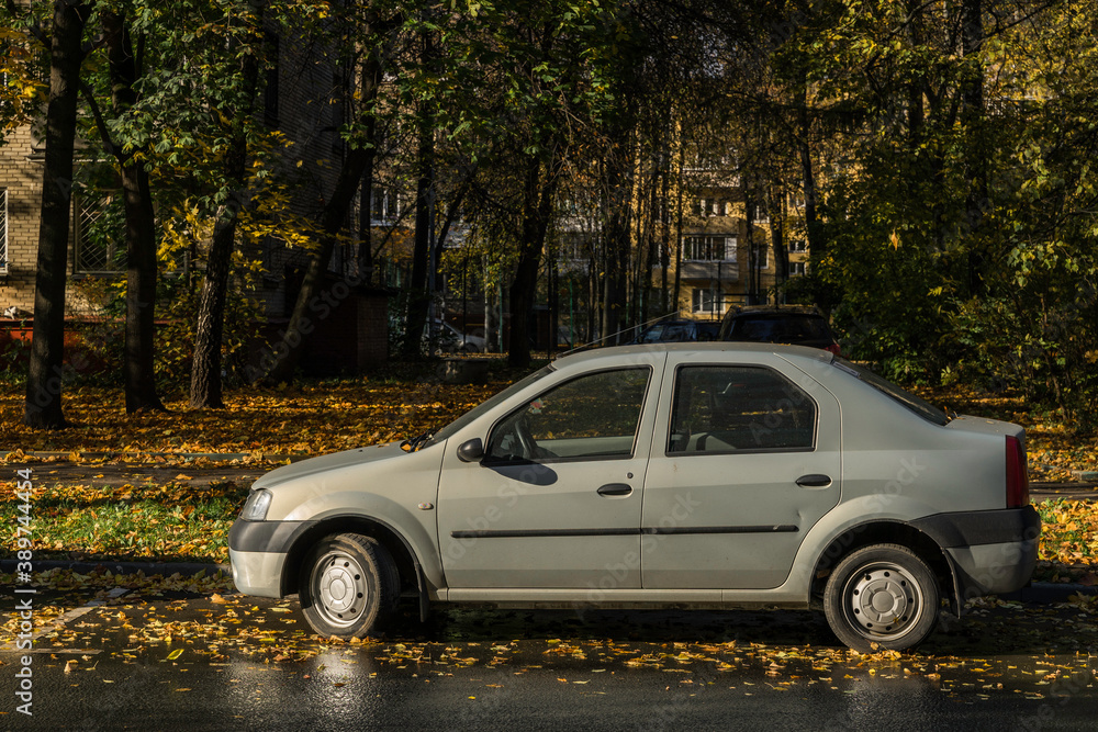 An old car is parked along the road in the afternoon in autumn weather among fallen and yellowed leaves