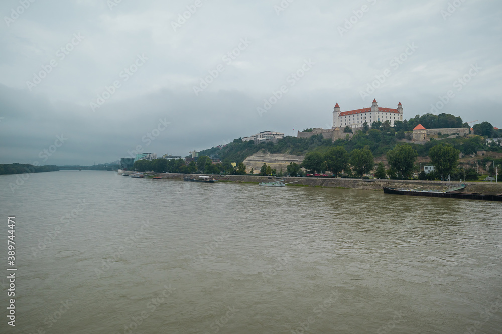 Moody panorama of Bratislava city viewed from the Novy bridge looking towards castle over the river on a dull grey day.