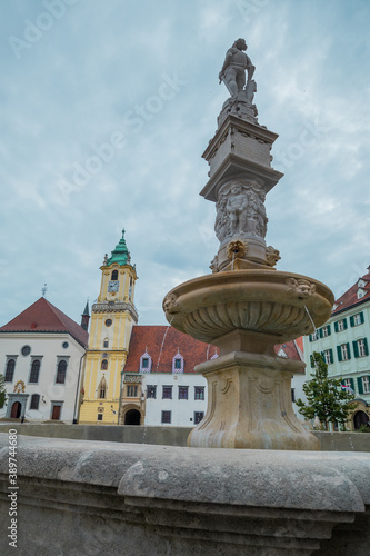 Maximilian fountain in Bratislava, Slovakia on the main Square of the city, with town hall seen in the background on a gray dull day.