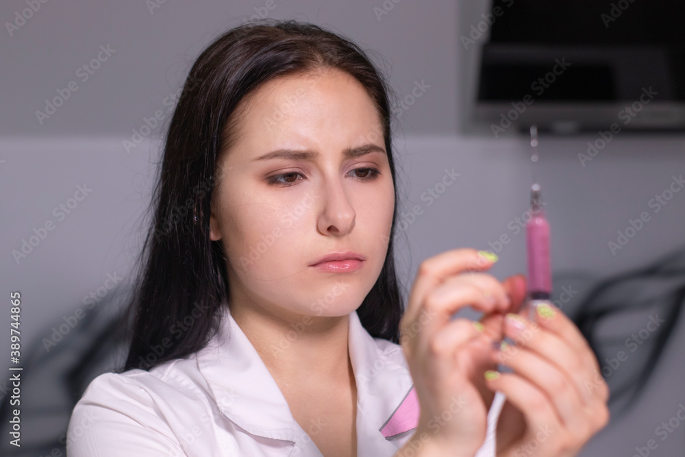 attractive brunette nurse in white and pink medical gown with a syringe in gray room. healthcare, coronavirus pandemic. attractive brunette nurse in white and pink medical gown with a syringe in gray room. healthcare, coronavirus pandemic.