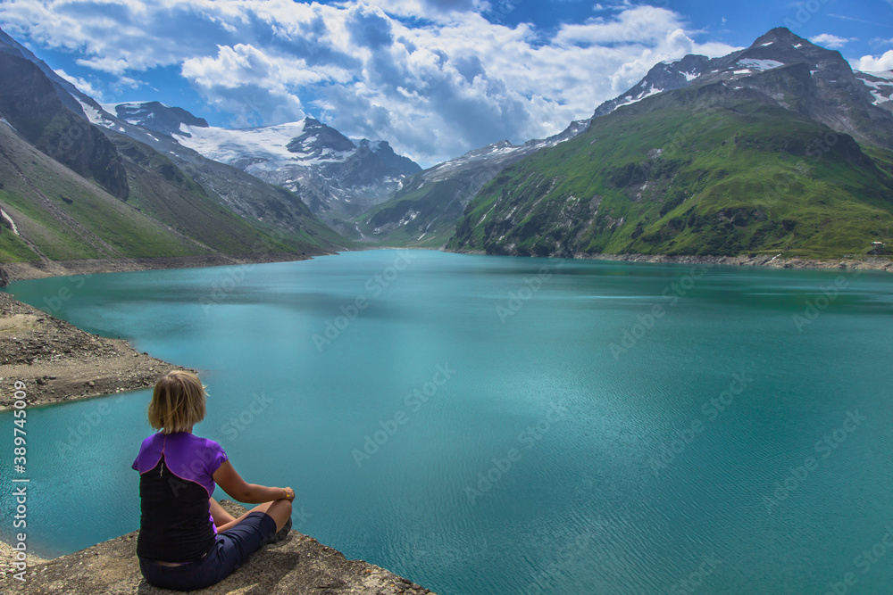Girl sitting on rock and enjoying beautiful view of high mountain lake near Kaprun.Quiet relaxation in nature.Wonderful nature landscape,turquoise water,holiday travel scene.Wanderlust background