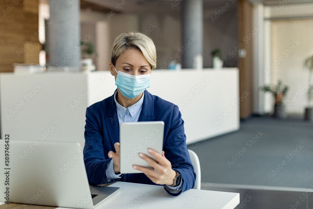 Businesswoman with protective face mask working on digital tablet in the office. Businesswoman with protective face mask working on digital tablet in the office.