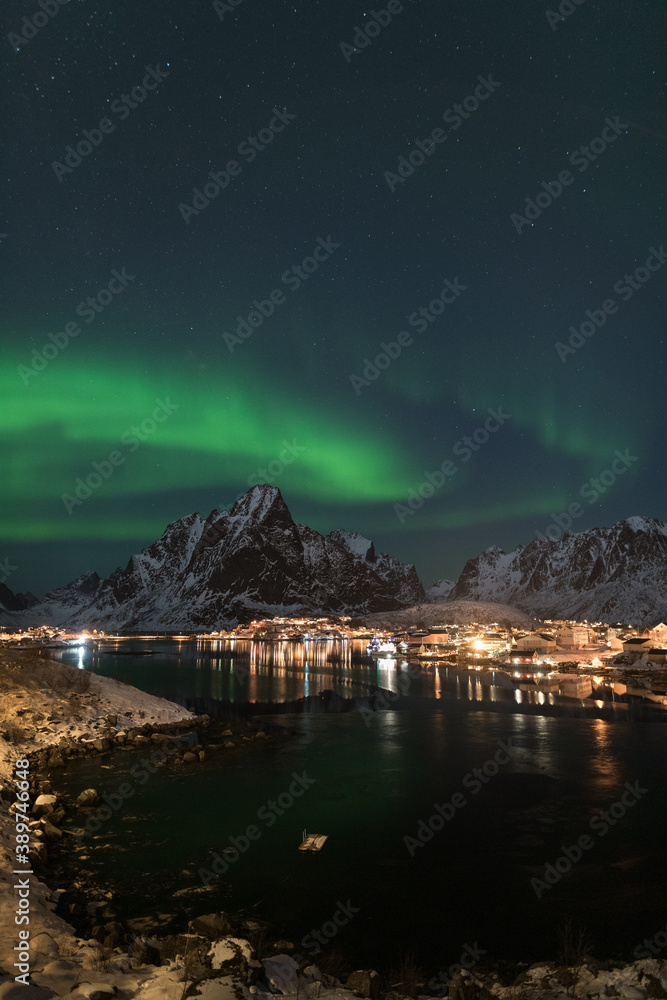 Dancing green polar lights over the village Reine on the Lofoten islands in Norway at night in winter with snow capped mountains