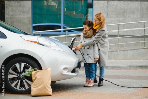 A stylish mother teaches her daughter how to properly charge an electric car
