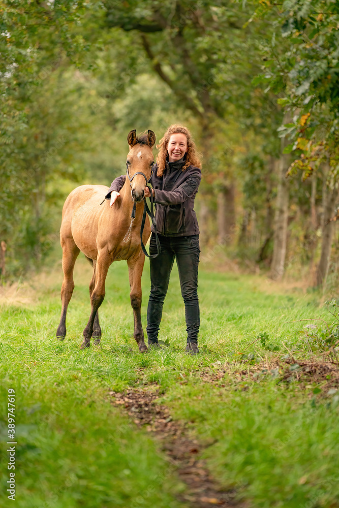 A light brown buckskin foal, the female owner stands next to the stallion Autumn Sun A light brown buckskin foal, the female owner stands next to the stallion Autumn Sun