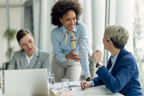 Happy African American businesswoman talking to female colleagues while working in the office.