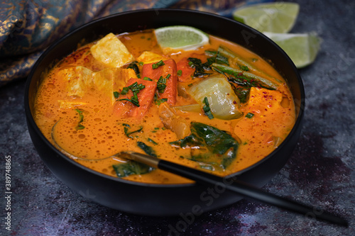 Vegan thai red curry with carrot, tofu and bock choy in black bowl, close up