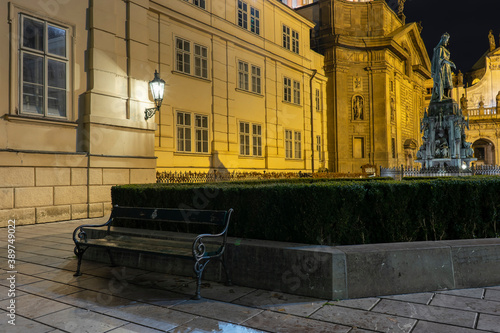 street lights and a bench and in the background a monument to Charles 4 from 1844 in the center of Prague near Charles Bridge at night