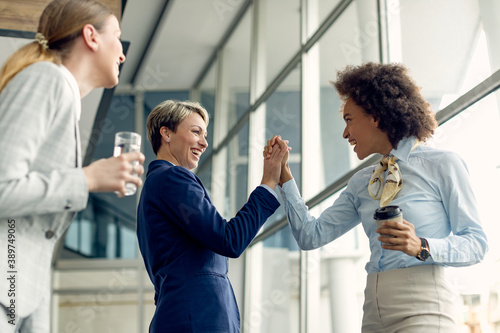 Happy businesswomen holding hands while greeting in a hallway.