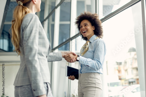 Happy black businesswoman handshaking with female colleague in a lobby.