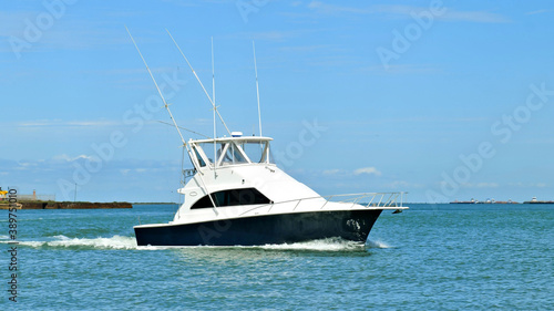Broadside view of a beautiful white and black fishing yacht boat sails left to right on the calm blue water on a sunny day.