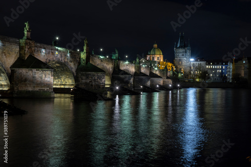  illuminated stone monument of karluv bridge from 14 century on river vltava and light from street lighting in the center of prague and prague architecture around