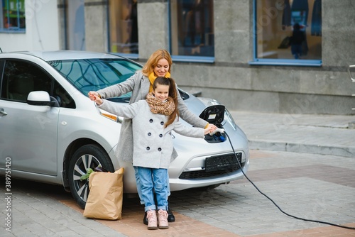 Stylish mother and daughter charge an electric car, and spend time together