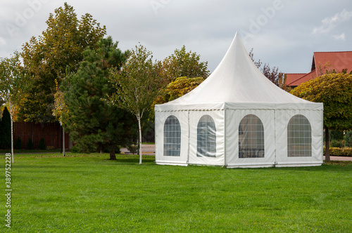 a white outdoor pavilion a on a green mowed lawn in the middle of the park