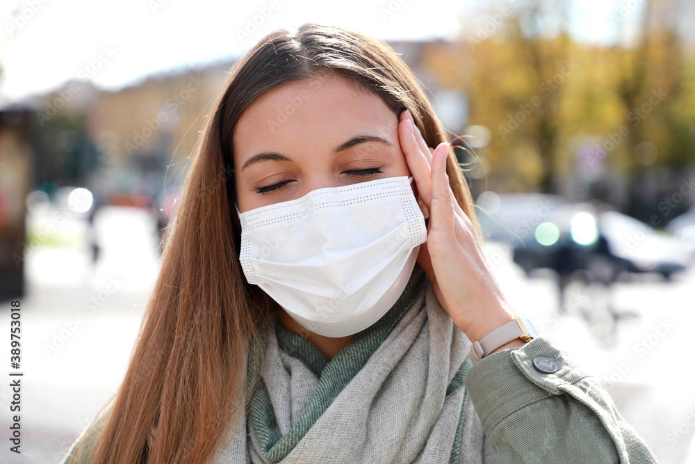 COVID-19 Close up of young woman in city street wearing white surgical mask suffers from headache COVID-19 Close up of young woman in city street wearing white surgical mask suffers from headache