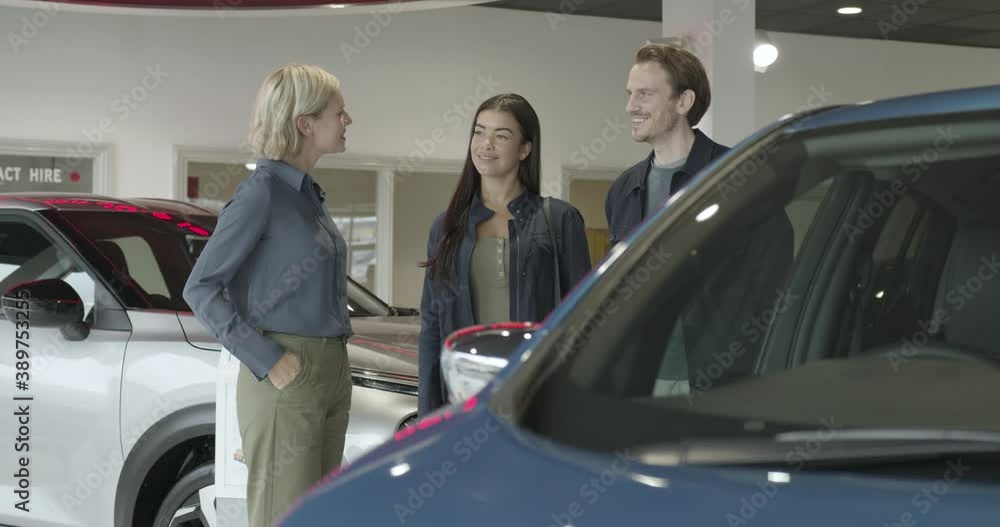Couple with saleswoman looking at electric car in automotive showroom Couple with saleswoman looking at electric car in automotive showroom