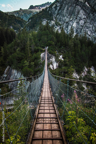 Fototapety na klatkę schodową  wooden-long-footbridge-above-the-deep-gorge-with-a-river-beach-at-the-bottom-between-the-rocks-wild-mountains-in-swiss-alps