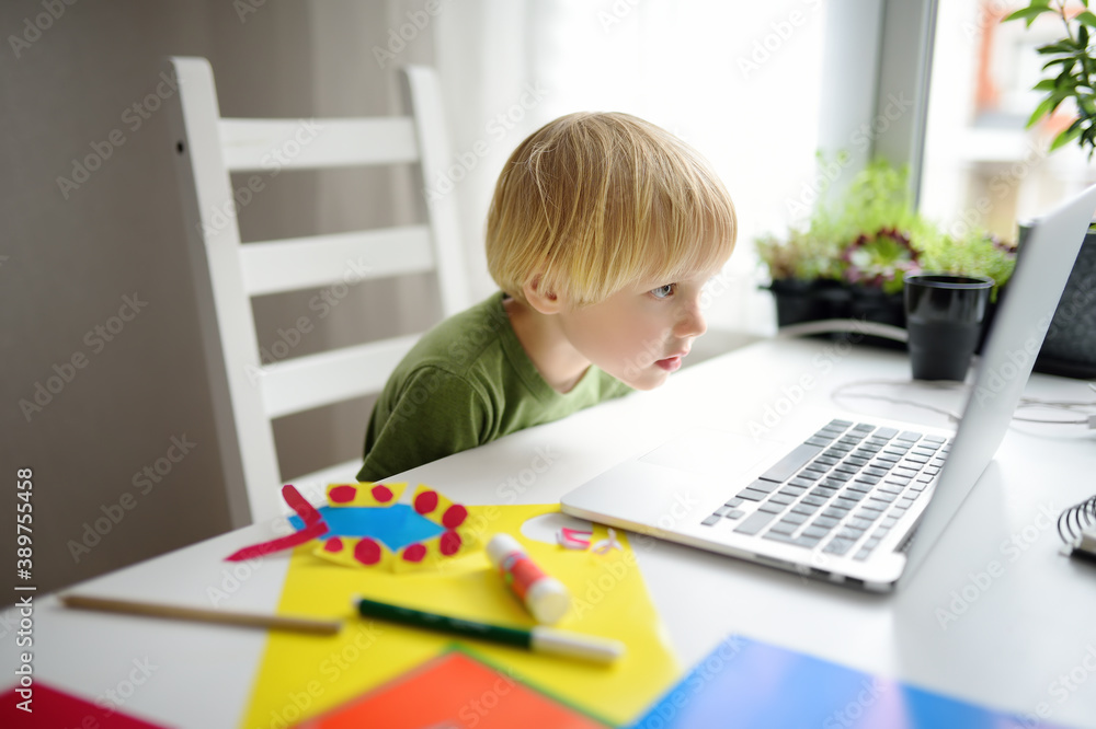 Child making colored paper crafts at home during coronavirus lockdown. Kid watching training video from Internet. Creativities lessons, distance learning, homeschooling, online kindergarten. Child making colored paper crafts at home during coronavirus lockdown. Kid watching training video from Internet. Creativities lessons, distance learning, homeschooling, online kindergarten.