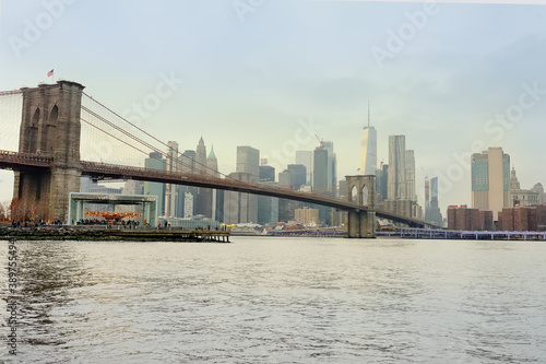 Stunning views of a famous suspended Brooklyn Bridge and Manhattan skyscrapers in New York from the riverside of the East River at a winter sunset. Sightseeing of NYC. © Maria Sbytova