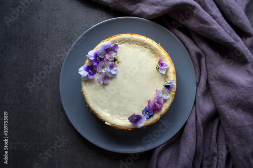 Fototapeta Naklejka Na Ścianę i Meble -  Homemade cheesecake decorated with blue wild pansy flowers. Top view photo on grey background with copy space.  
