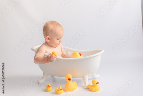 small child bathes in a white tub with rubber ducks and foam