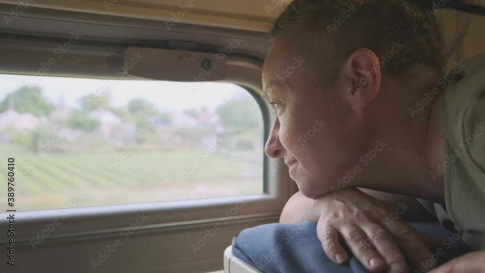 woman passenger looks out window while riding train lying on top shelf in compartment. woman passenger looks out window while riding train lying on top shelf in compartment.