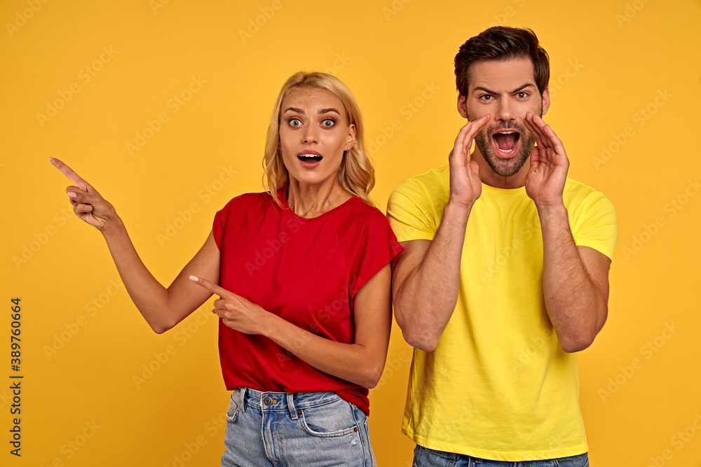 Shocked young couple friends guy girl in t-shirts isolated on yellow background studio. People lifestyle concept. Mock up copy space. Pointing index fingers aside up, put hands on cheeks. Shocked young couple friends guy girl in t-shirts isolated on yellow background studio. People lifestyle concept. Mock up copy space. Pointing index fingers aside up, put hands on cheeks.