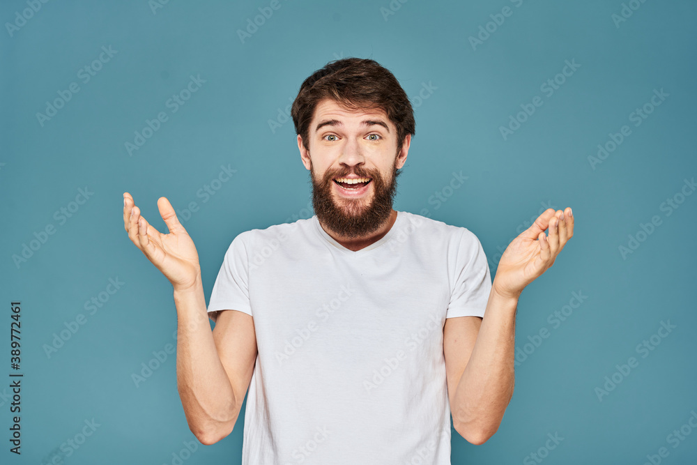 A bearded man in a white T-shirt gestures with his hands emotions blue background A bearded man in a white T-shirt gestures with his hands emotions blue background