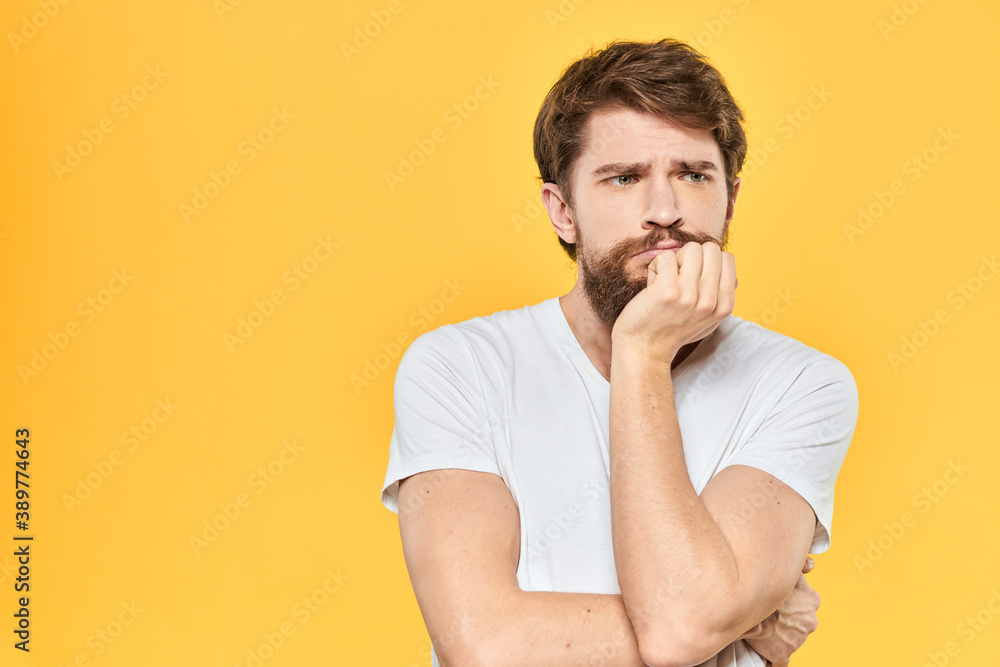 Bearded man in a white T-shirt gestures with his hands emotions studio yellow background Bearded man in a white T-shirt gestures with his hands emotions studio yellow background