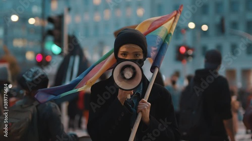 Woman with face mask speaking into the megaphone while holding rainbow flag. Demonstration against dicrimination . High quality 4k footage photo