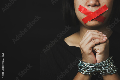 Asian woman blindfold wrapping mouth with red adhesive tape and she was hand tethered on black background. Freedom speech censorship and stop talk, International Human Right day photo
