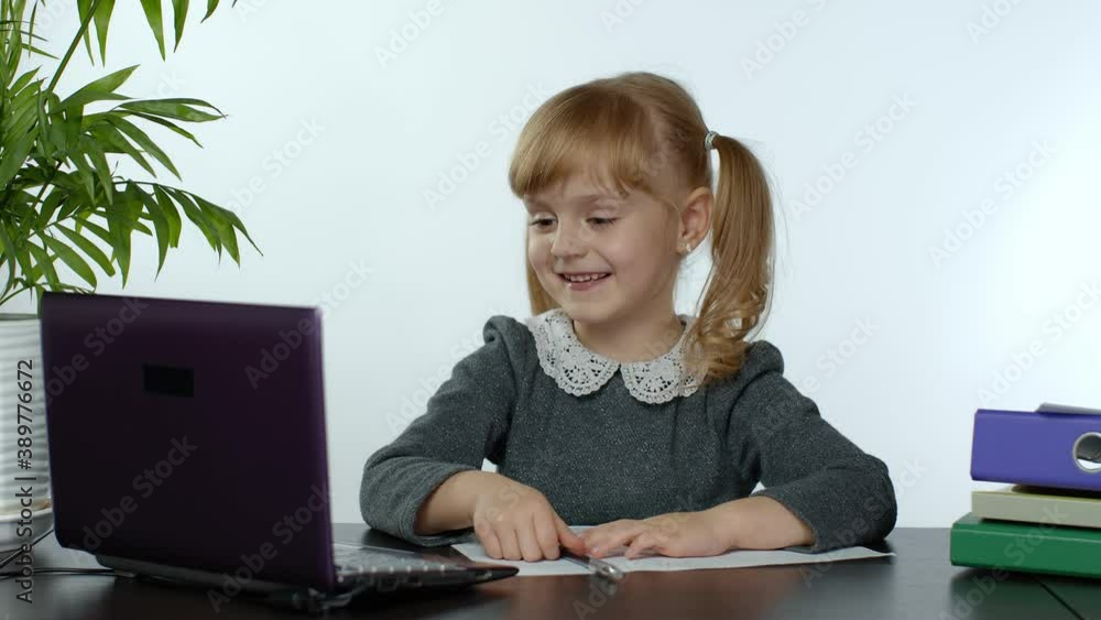 Child schoolgirl learns lessons at home sitting at table using digital laptop computer. Portrait of kid girl distance education. Studying during coronavirus quarantine. White background. 6k downscale Child schoolgirl learns lessons at home sitting at table using digital laptop computer. Portrait of kid girl distance education. Studying during coronavirus quarantine. White background. 6k downscale