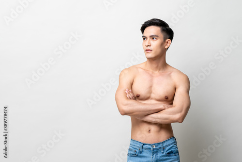 Portrait of handsome shirtless Asian man looking at the side with arms crossed in isolated studio light gray background