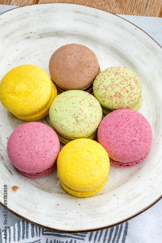 Multicolored macarons on a plate and wooden background Multicolored macarons on a plate and wooden background
