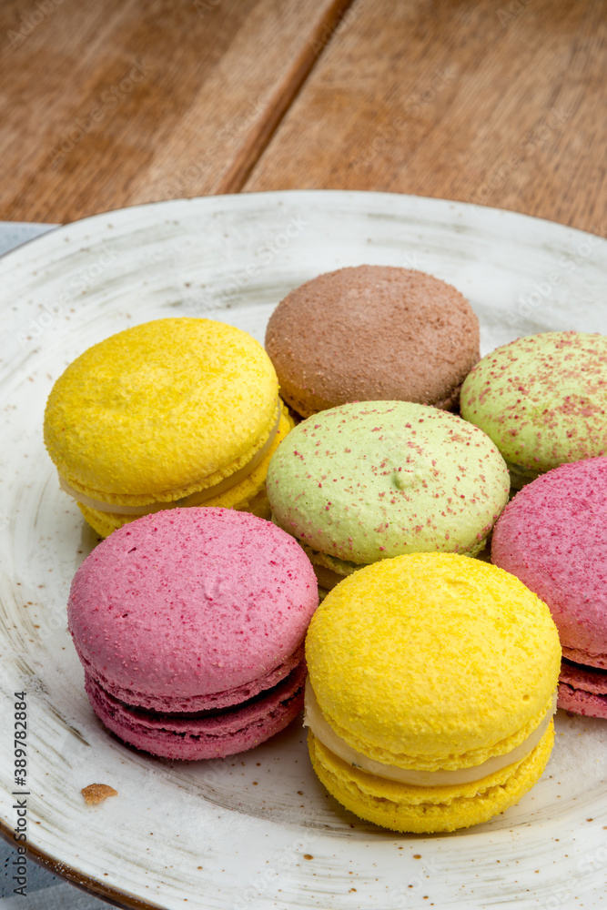 Multicolored macarons on a plate and wooden background Multicolored macarons on a plate and wooden background