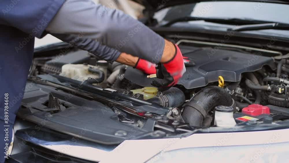 Car mechanic under repairing car open hood checking oil motor level for refill and clean in car garage service. Car mechanic under repairing car open hood checking oil motor level for refill and clean in car garage service.