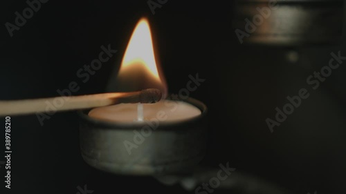 Close up of a tealight in a silver candleholder being lit by a flaring match stick with a dark background a night. Shot in 4K. photo