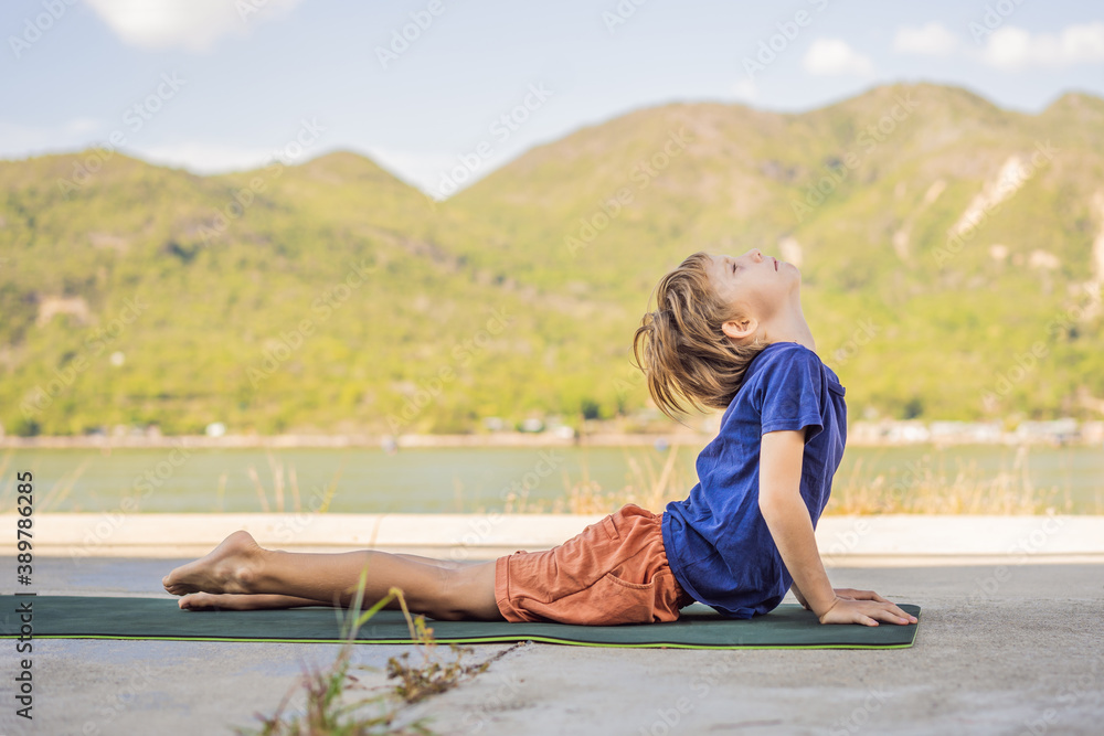 Fototapeta premium Boy doing yoga on a yoga mat against a background of mountains
