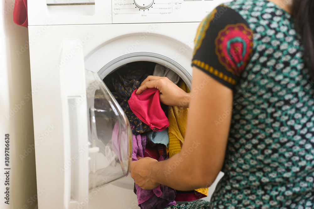 Woman doing laundry , hand loading soiled clothes into front load