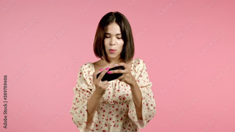 Woman playing game on smartphone on pink studio wall. Using modern technology - apps, social networks. Woman playing game on smartphone on pink studio wall. Using modern technology - apps, social networks.