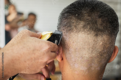 Asian young man who have gray hair being haircut with electric clipper machine by professional barber in barbershop.