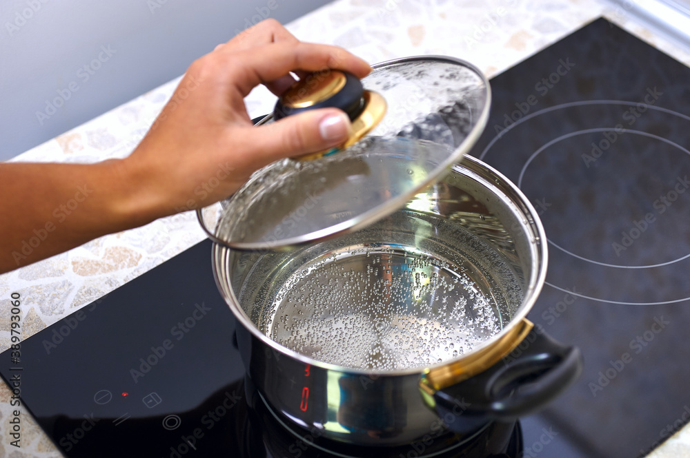 Women hand open a saucepan in modern kitchen with induction stove Women hand open a saucepan in modern kitchen with induction stove