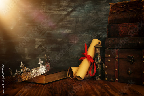 low key image of beautiful queen/king crown, old books and feather quill ink pen over wooden table. fantasy medieval period © tomertu