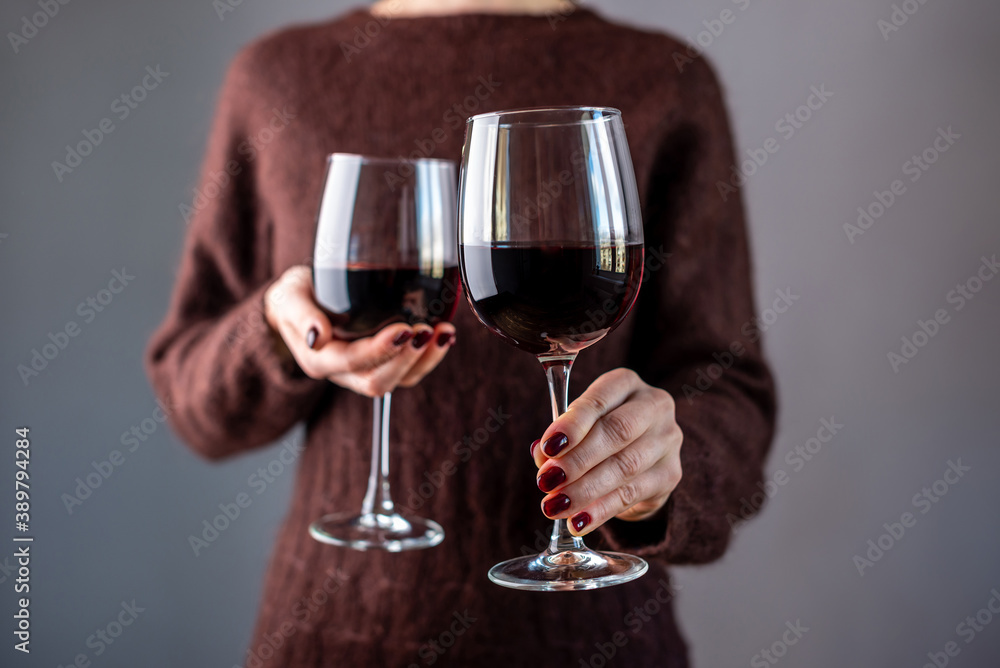 A woman in a brown sweater is holding two glasses of red wine and holding out one of them. Close up A woman in a brown sweater is holding two glasses of red wine and holding out one of them. Close up